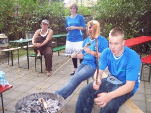 Jugendliche backen Stockbrot über dem Holzkohlengrill.